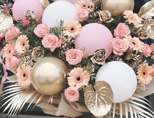 6 Pink Gold and White balloons  placed in between gold leaves and 20 pink roses and gerberas